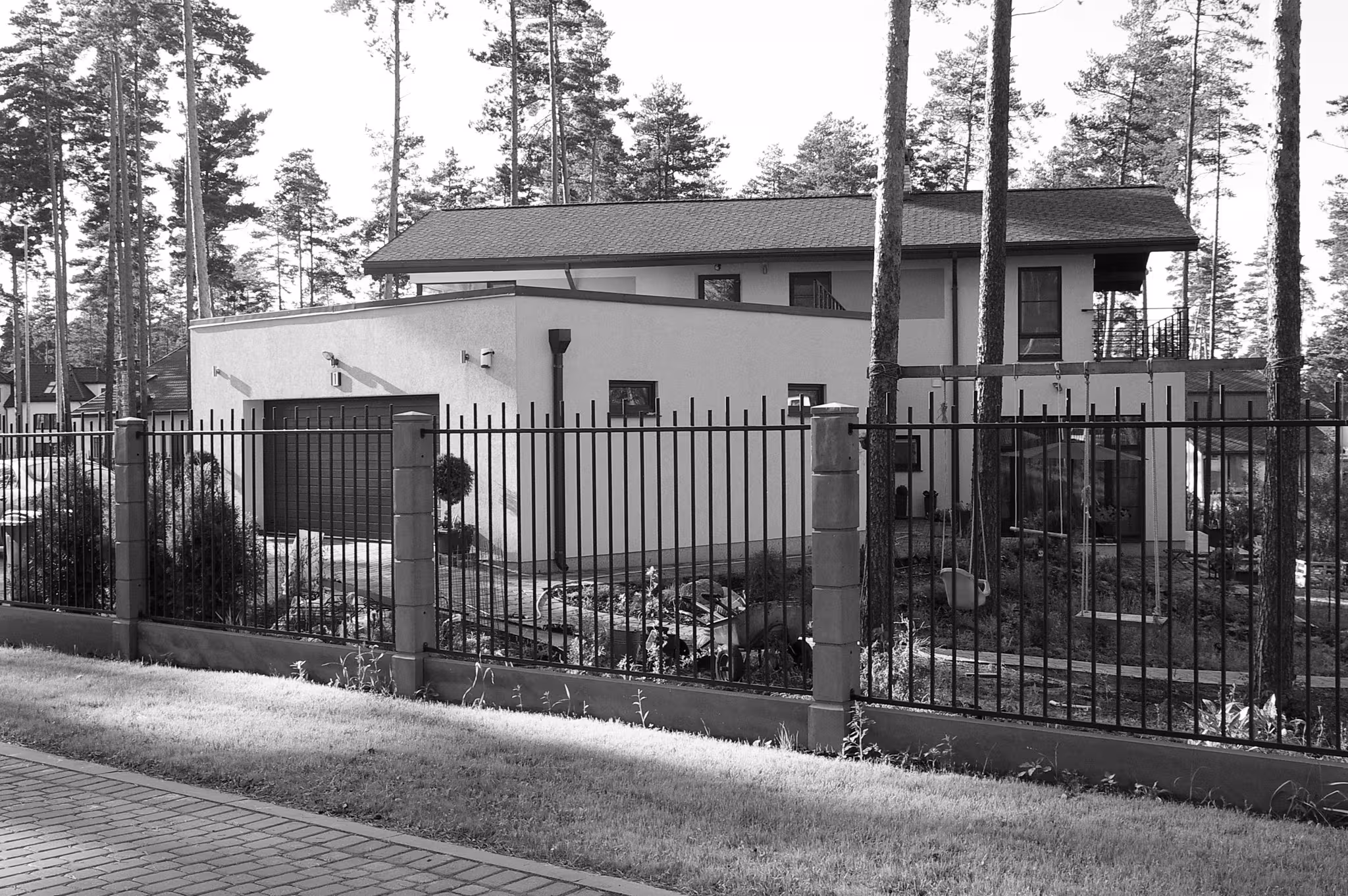 Modern residential architecture with a two-story house, integrated garage, and a dark fence amidst tall pine trees.