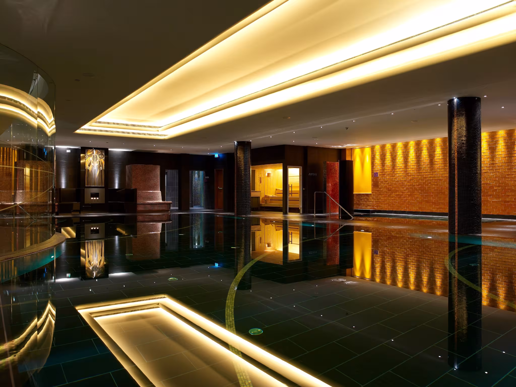 Luxury black mosaic swimming pool at E’SPA Riga with textured gold colored walls and mood lighting reflecting on the water surface.