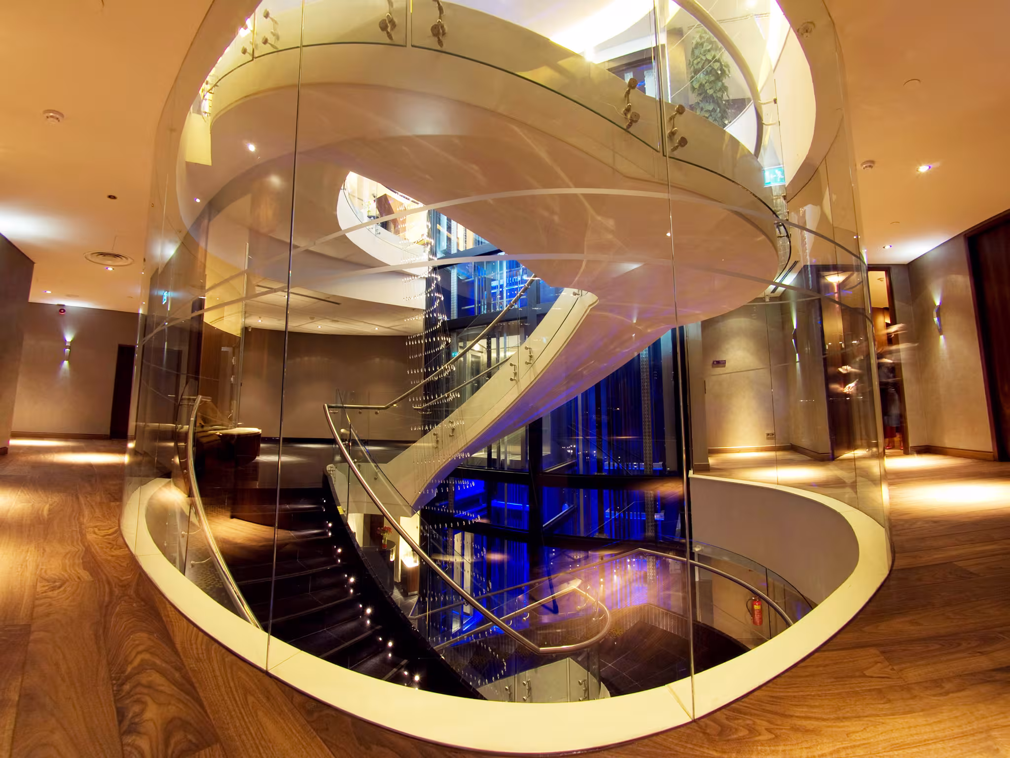 Sculptural spiral staircase with glass balustrades serving as the vertical spine of the E’SPA Riga wellness center.