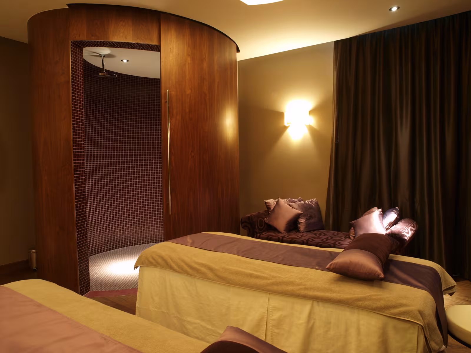 Double treatment room at E’SPA Riga with curved walnut veneer walls and soft lighting creating a cocoon-like atmosphere.