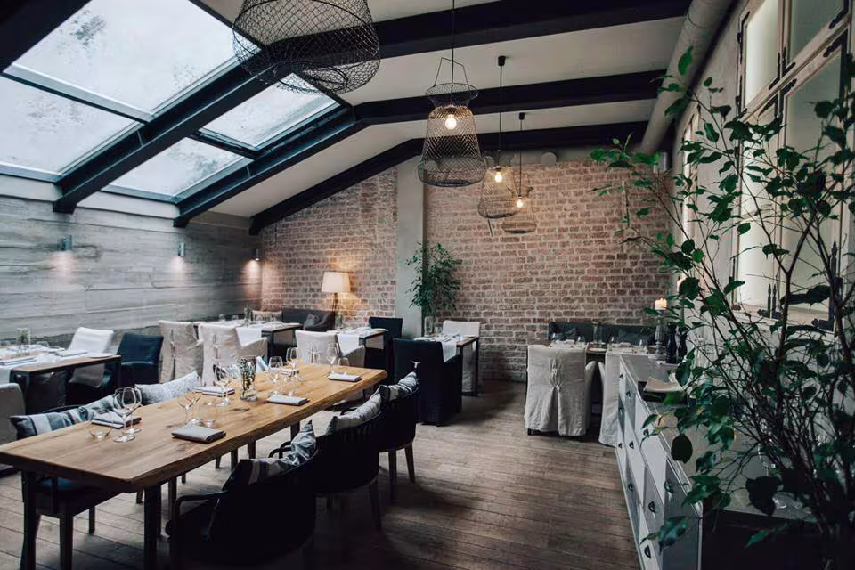 Restaurant interior featuring a new glass roof structure that creates a bright "winter garden" effect within the historic brick walls.