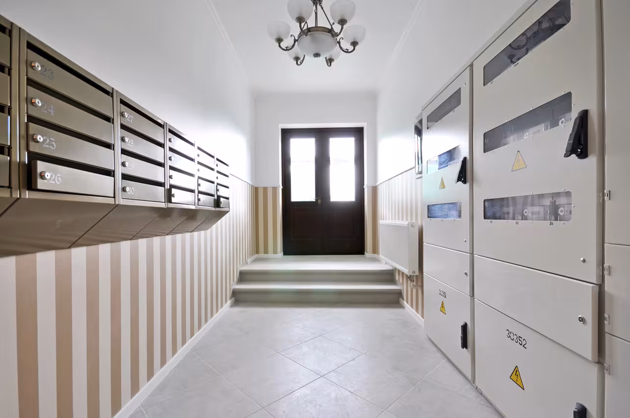Renovated common hallway area with modern mailboxes, utility cabinets and classic striped wallpaper design at 5 Alīses Street apartments.