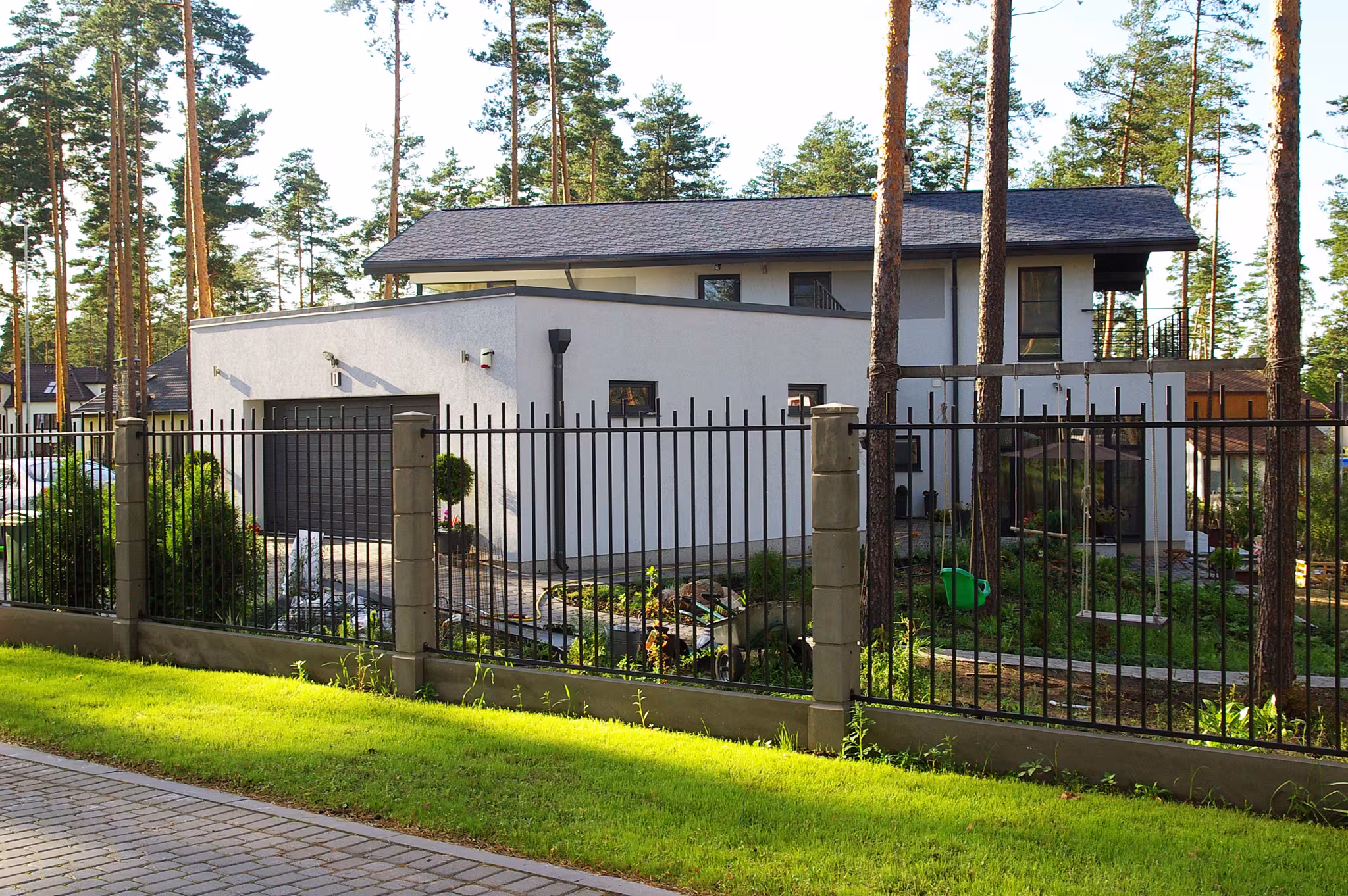 Modern private house façade detail with white plaster walls and window openings set within a pine forest environment