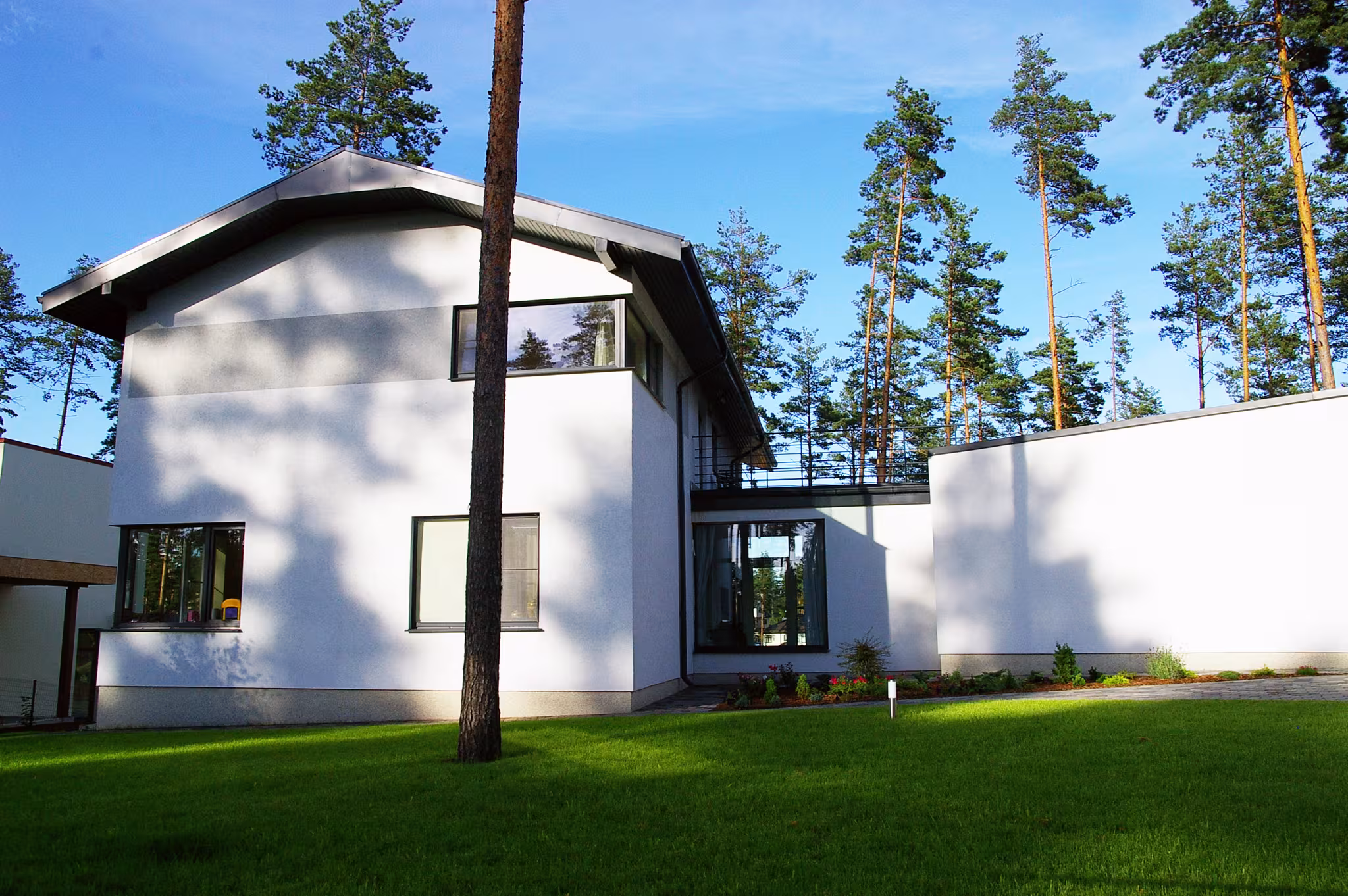 Two storey private residence in a pine forest with white plaster façade, dark roofline and large windows opening toward the landscape