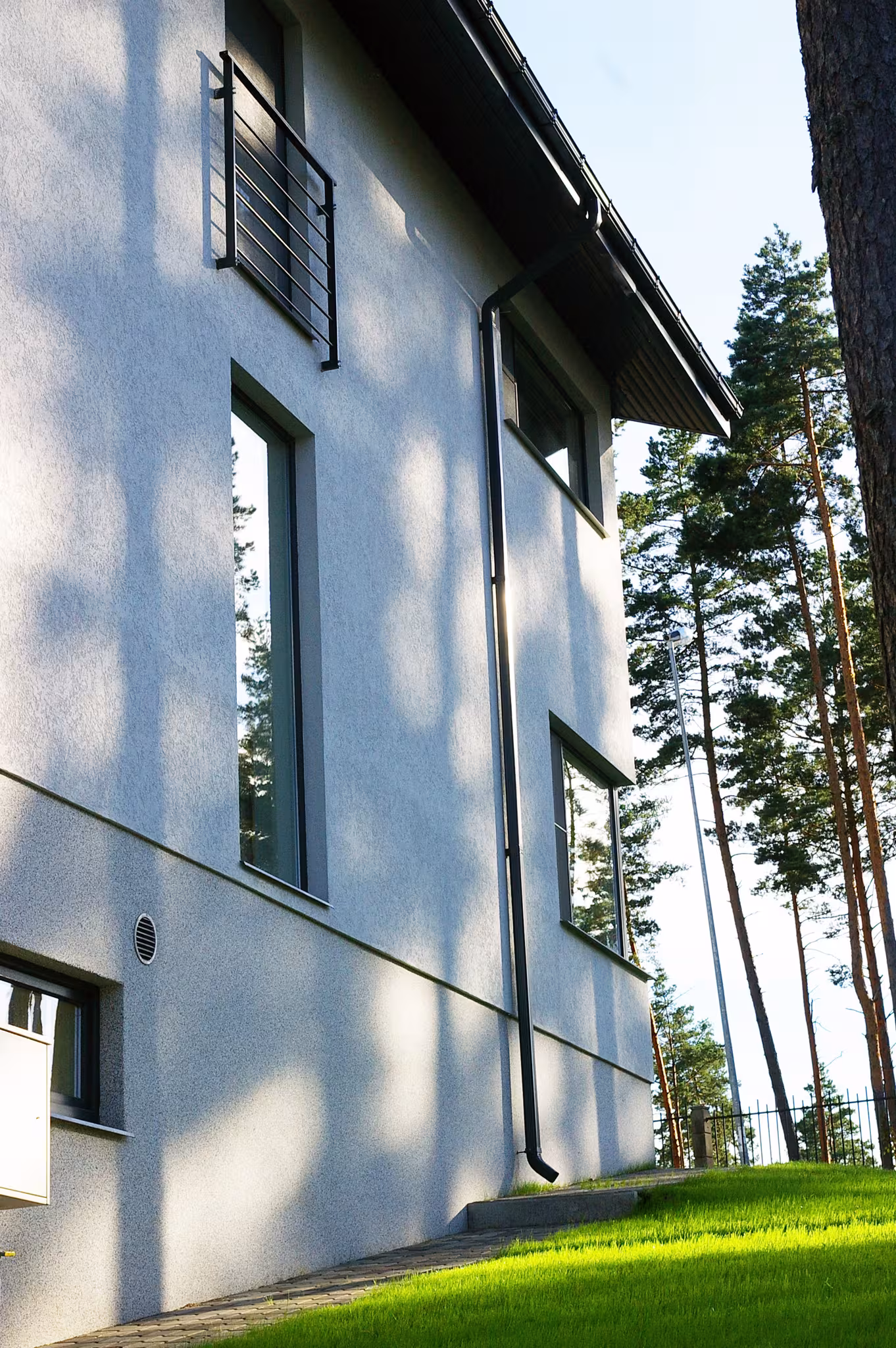 Rear garden view of the private house in Ezerkrasti, highlighting the glass link volume connecting the main house and auxiliary block within a forest setting