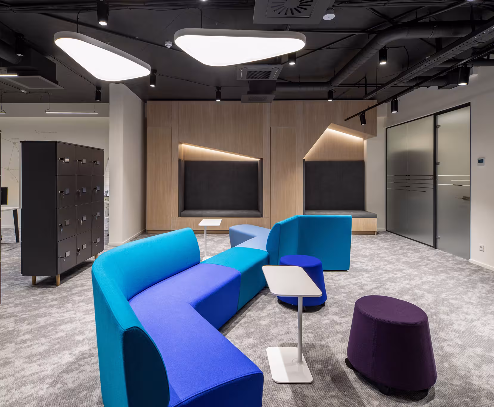 Dynamic circulation area featuring a curved blue and purple modular sofa, employee lockers and triangular ceiling lights to encourage social interaction.
