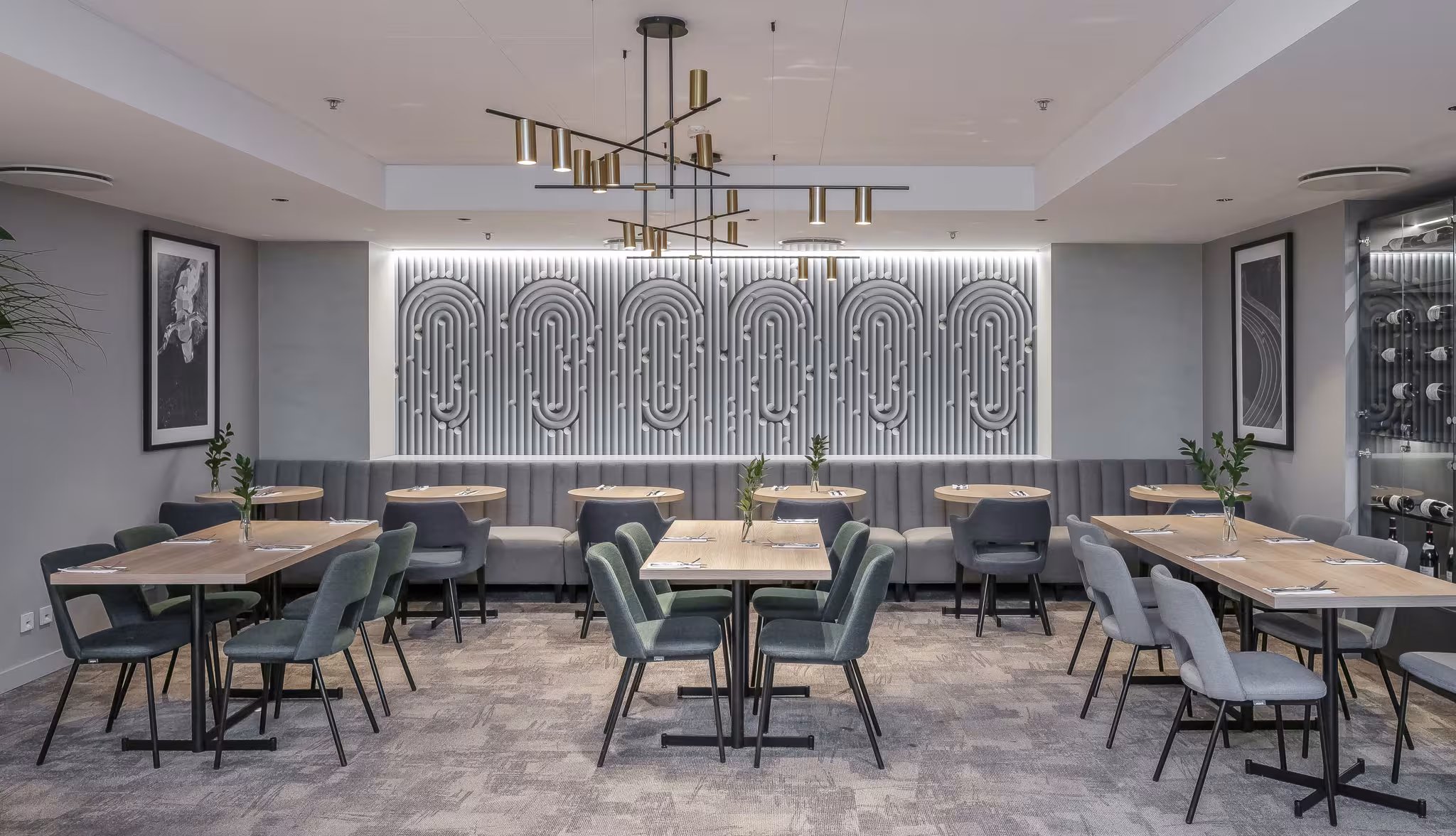 Contemporary restaurant interior with moss green chairs, light wood tables and a decorative grey acoustic wall feature with geometric patterns.