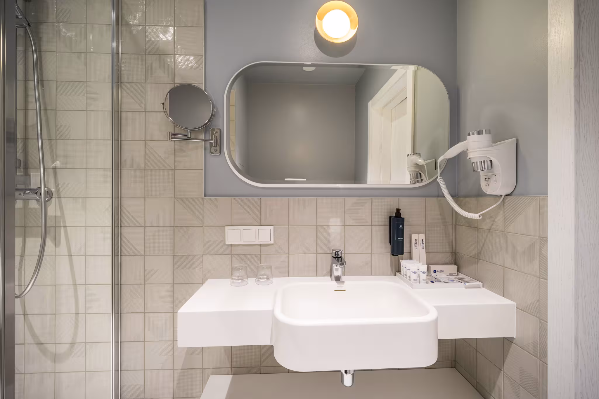 Riverside SPA Hotel's bright bathroom features a modern sink, large mirror, hairdryer, and glass shower.