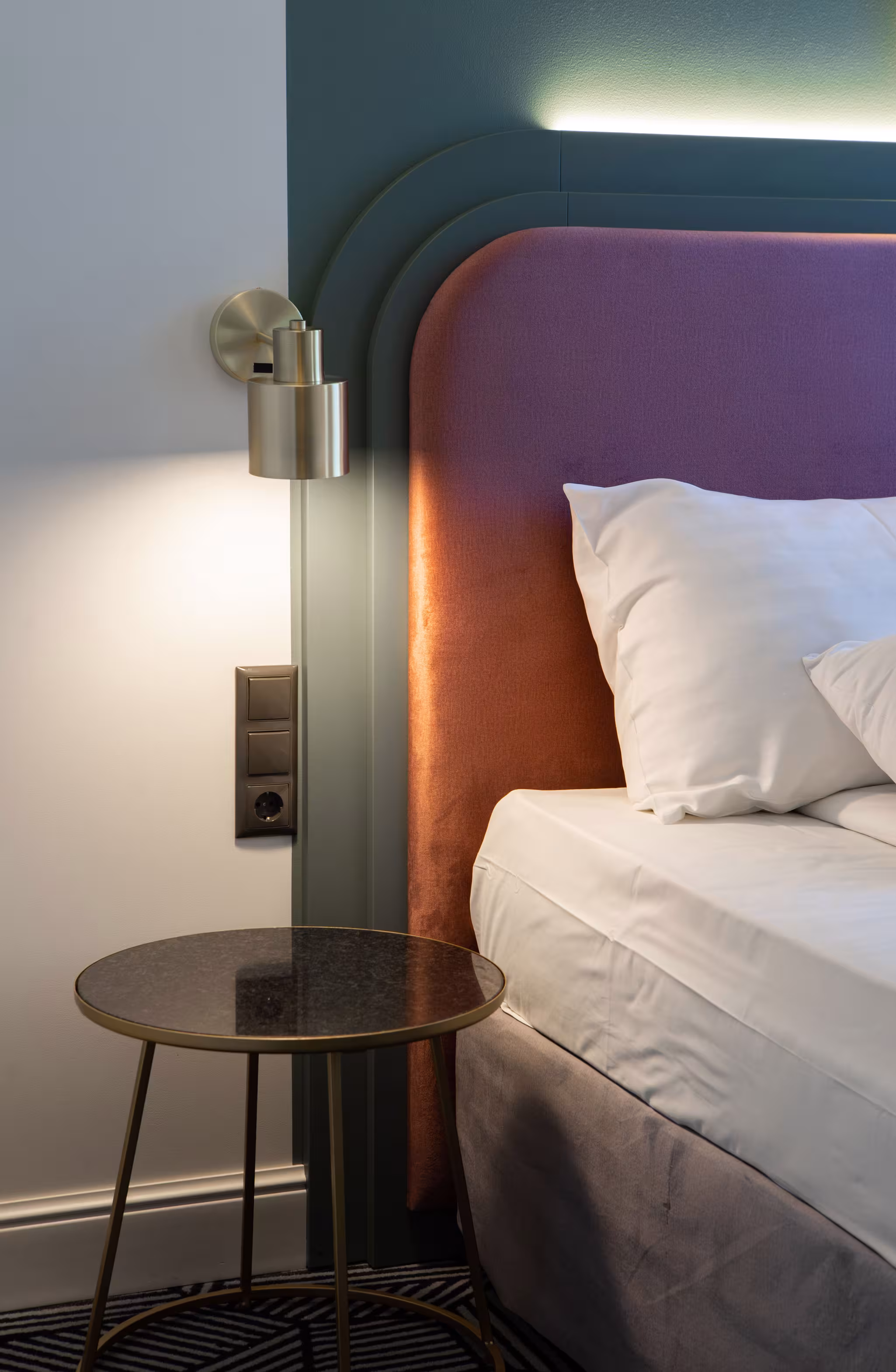 Riverside SPA Hotel modern bedside with gold lamp, round table, and colorful headboard.
