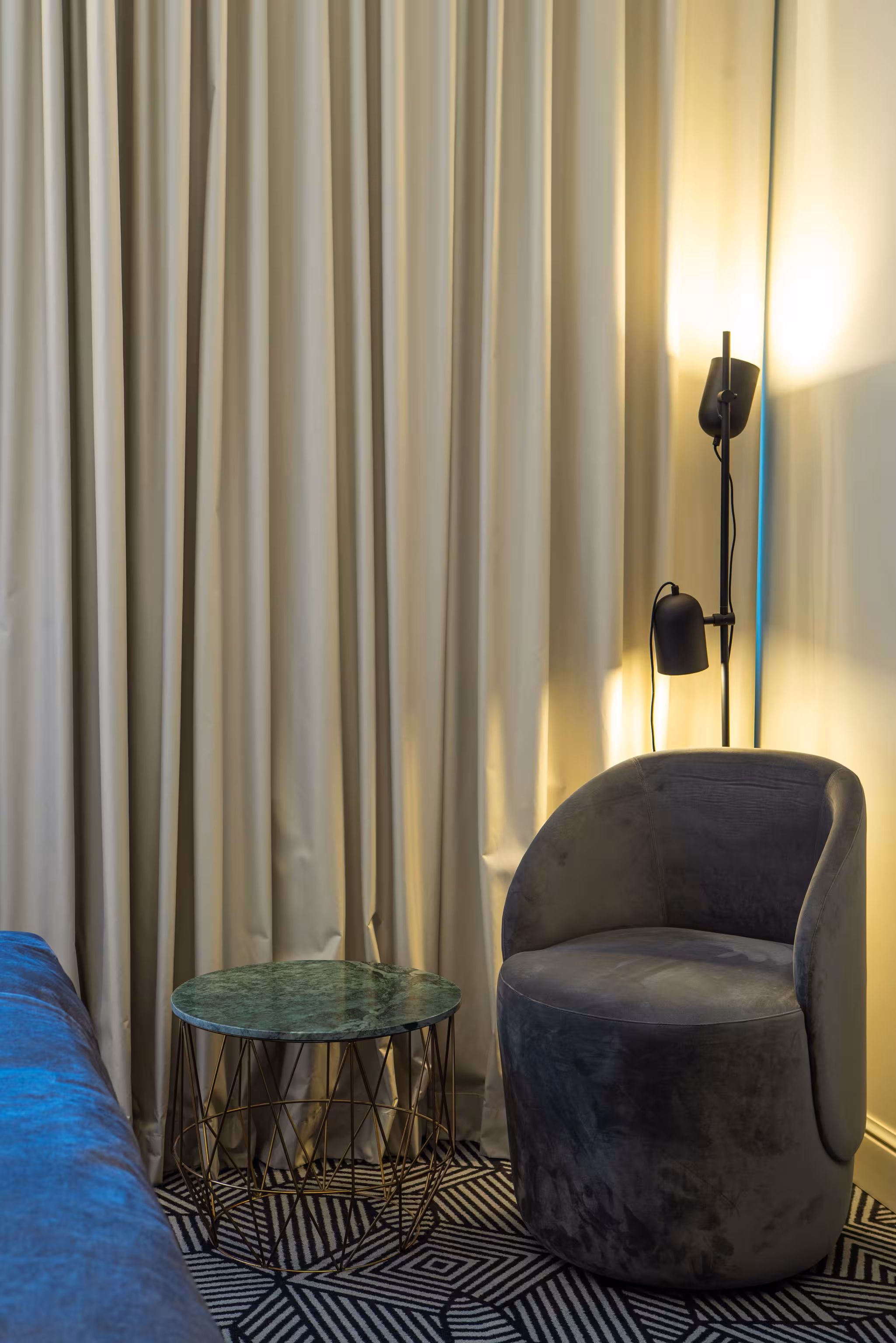 Cozy corner in Riverside SPA Hotel room with a velvet armchair, unique side table, and warm lamp.