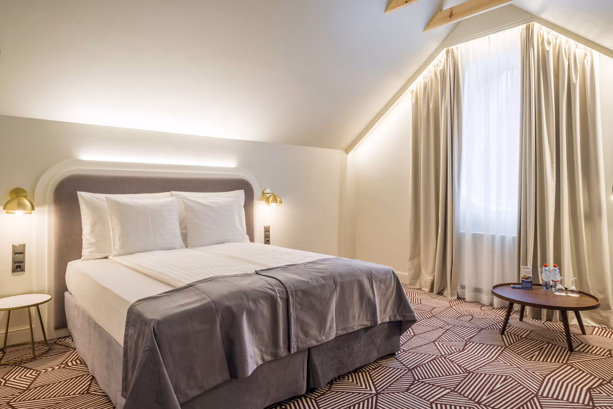 Elegant double room at Riverside SPA Hotel with a large bed, warm lighting, and a sloped ceiling.
