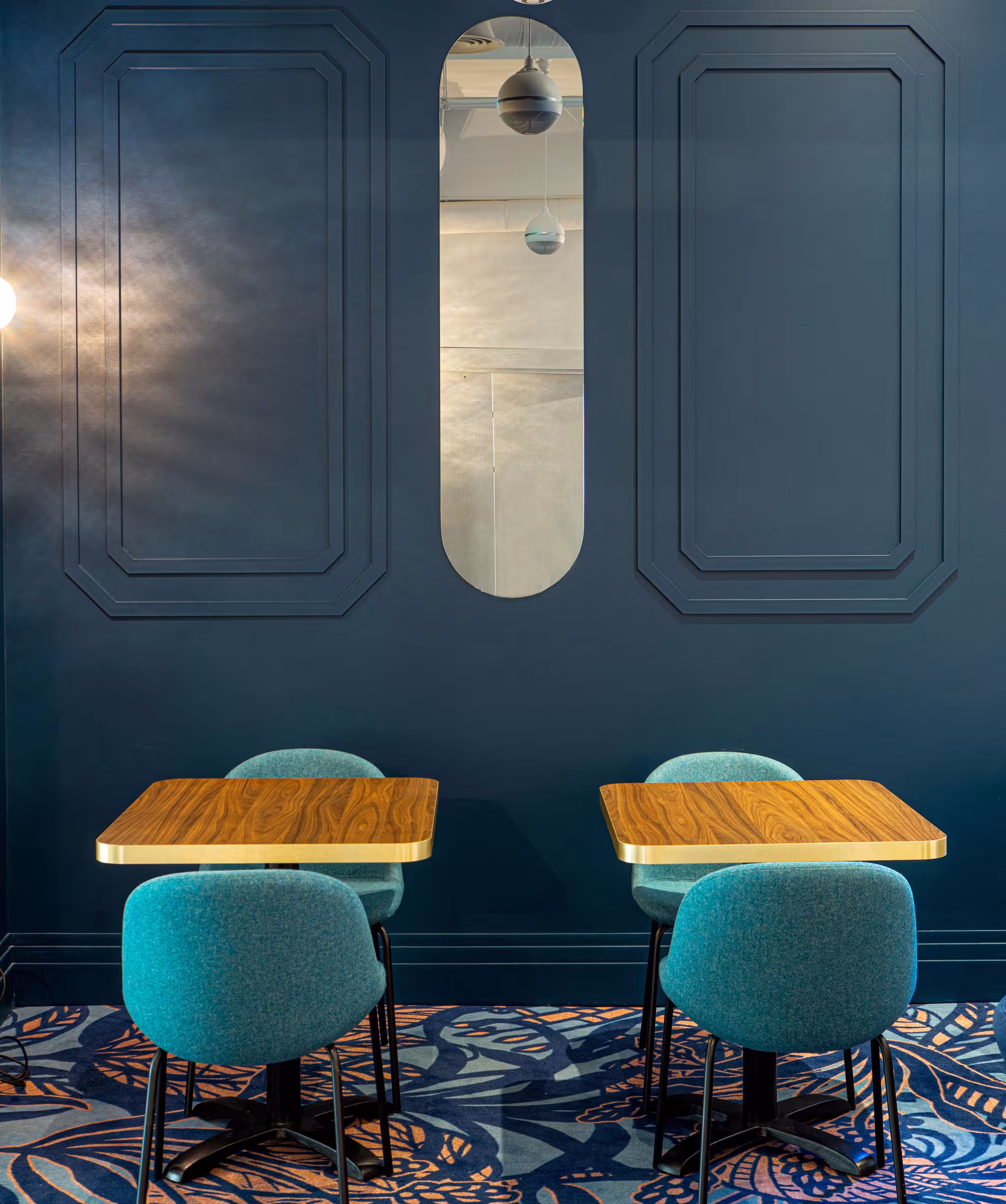 Riverside SPA Hotel lounge with two tables, teal chairs, patterned carpet, and blue wall.