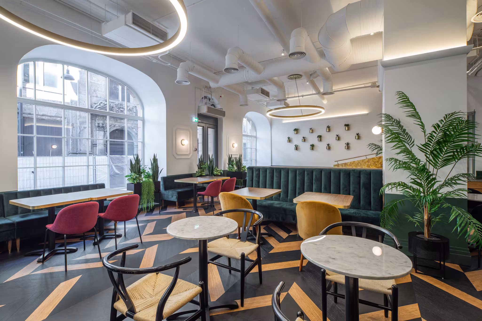 Modern dining interior at Riverside SPA Hotel featuring green velvet booths, marble tables, and large arched windows.
