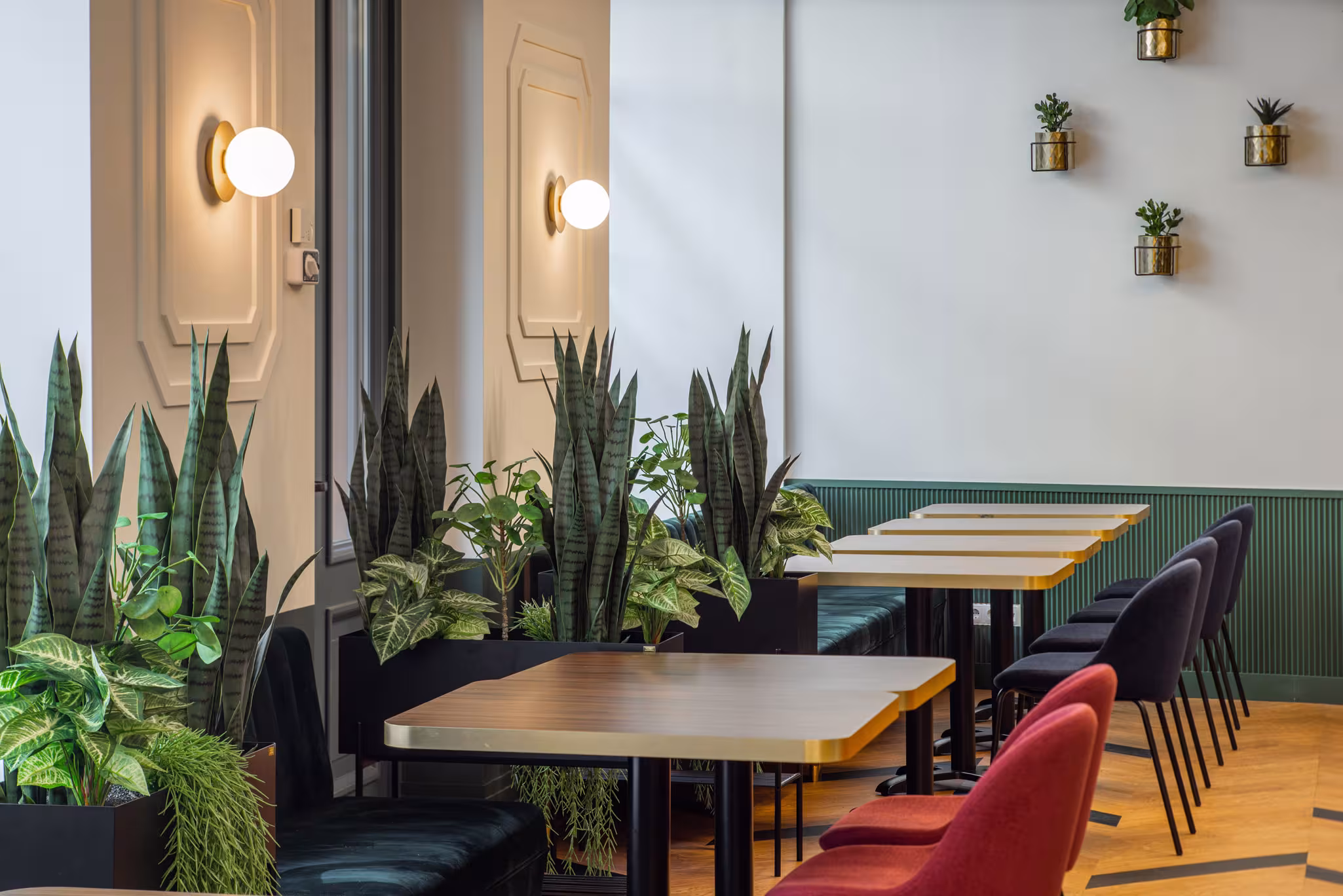 Modern dining area at Riverside SPA Hotel. Gold-top tables, velvet chairs, green plants, and wall decor.